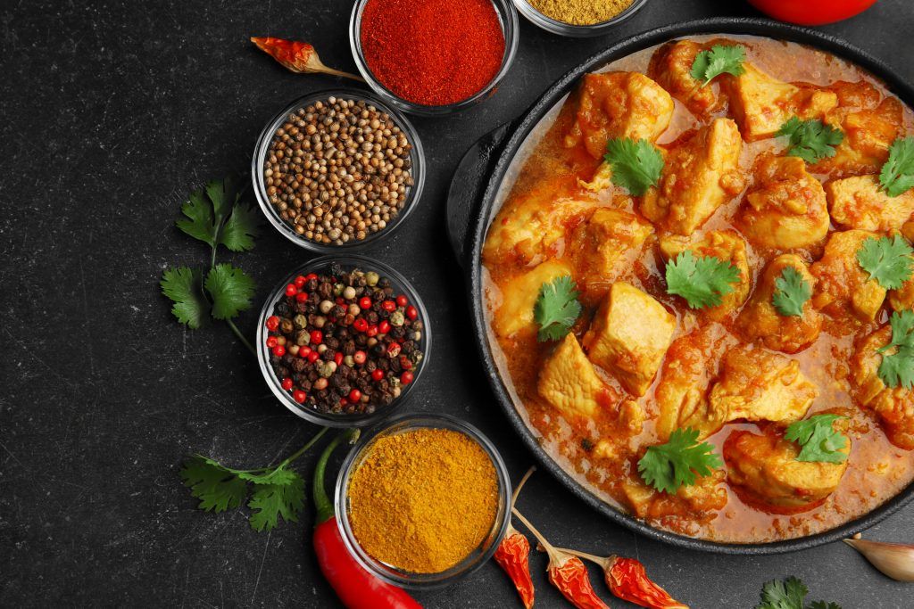 Chicken curry surrounded by bowls of whole spices