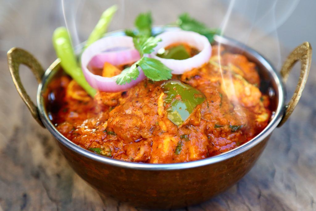 Steaming curry in a copper karahi, topped with onion, green chilli and coriander